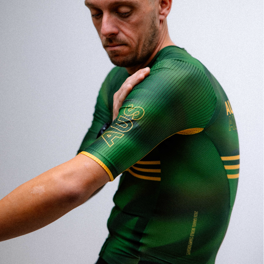 A man wearing a green and gold athletic jersey with 'AUS' printed on the sleeve, posing in a studio setting against a plain light gray background.
