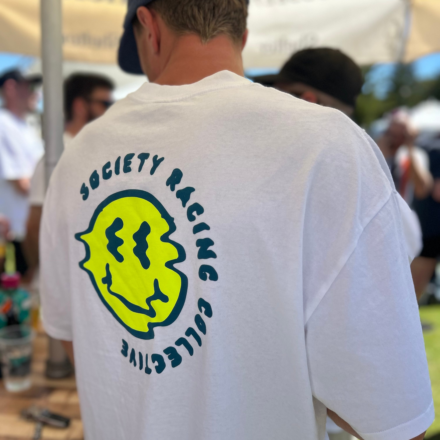Person wearing a white t-shirt with a logo and text, standing outdoors.
