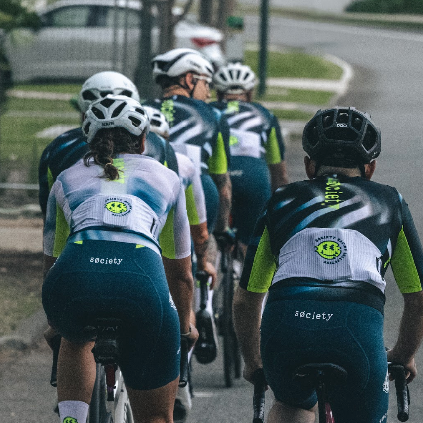 Group of cyclists riding on a road with visible branding on their uniforms.