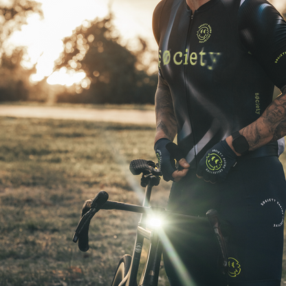 Cyclist in black and green cycling gear with a helmet, holding a bike in a natural setting.
