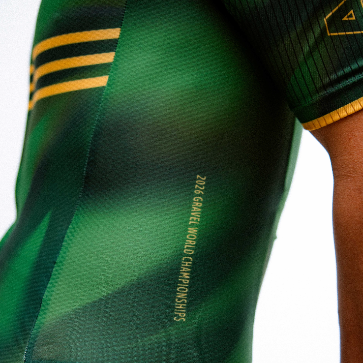 Close-up of a person wearing a green cycling jersey with gold stripes, gold trim, and gold lettering on the sleeve, paired with black cycling shorts.